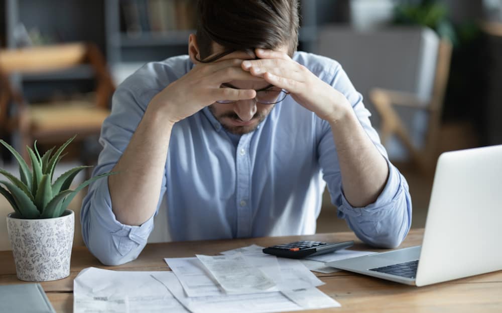 Sad depressed man checking bills, anxiety about debt or bankruptcy, financial problem, bank debt or lack of money, unhappy frustrated young male sitting at work desk with laptop and calculator
