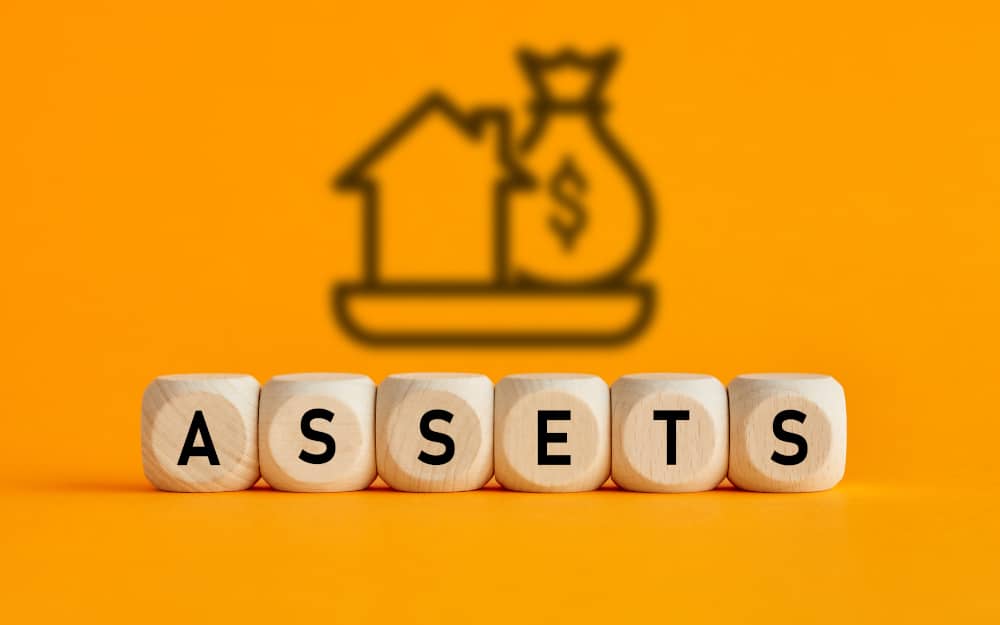 The word assets written on wooden cubes with assets icon on yellow background. Asset management or financial accounting concept.